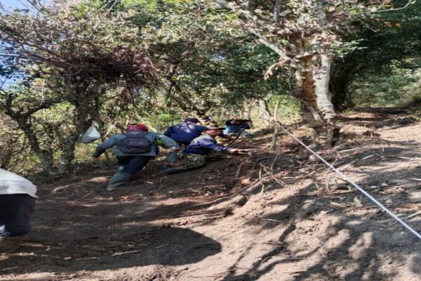 Puluhan warga Dusun Bendorejo, Desa Sumberagung, Ngantang, bekerja bakti membuka jalur pendakian di lereng Puncak Srege. Mereka membawa cangkul dan sekop, dengan latar belakang perbukitan hijau dan Waduk Selorejo yang terlihat di kejauhan.